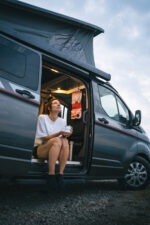 Une personne est assise sur le marche pied de son van avec la poche intérieure du sac de voyage Neo Sambuy Nomad accroché au plafond du van