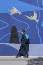 Un homme marche devant un mur peint avec le Sac de voyage Neo Sambuy Sport