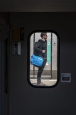A travers la fenêtre d'un train, on voit un homme sur le quai qui attend avec son sac de voyage Neo Sambuy Sport
